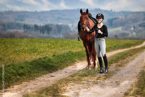Rider and horse stand side by side on a path in a wide spring landscape. © RD-Fotografie