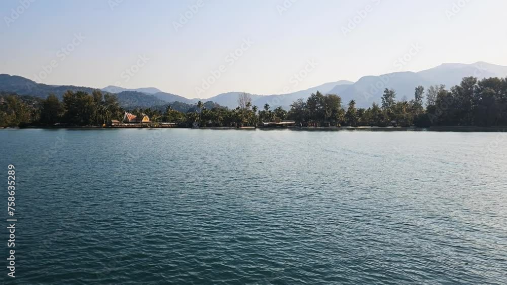 Sunlit tropical coastline of Koh Chang with gentle waves and a clear sky, framed by lush greenery and mountains Sunlit tropical coastline of Koh Chang with gentle waves and a clear sky, framed by lush greenery and mountains
