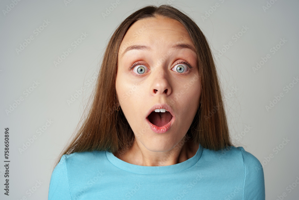 Young pretty surprised woman with opened mouth standing on gray background Young pretty surprised woman with opened mouth standing on gray background