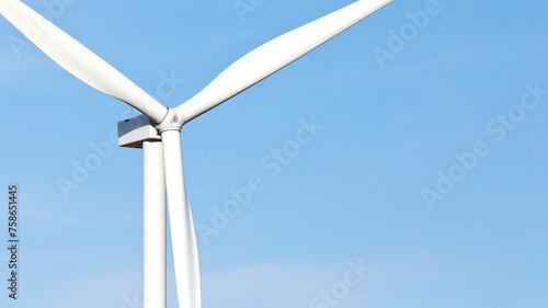 Close-up color photo of large wind turbine blades against a blue sky background with copy space.