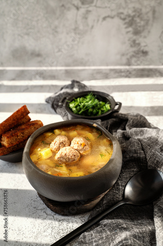 Meatball in a spoon. soup with meatballs in a black bowl and croutons in hard light. A European dish typical of Spain, Sweden, Turkey, and Russia. Meatballs, kyufta, faggots - meat balls in soup photo