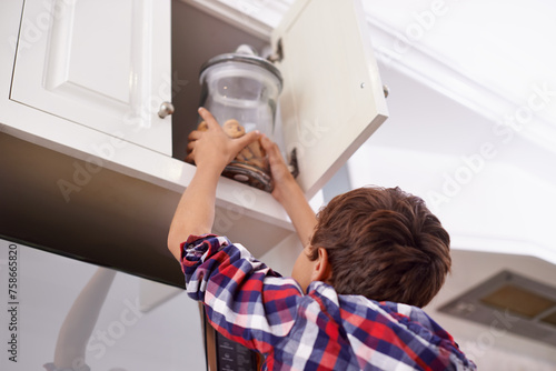 Fotografija Kitchen, cupboard and cookie jar with boy child reaching for treats for hunger in home from below