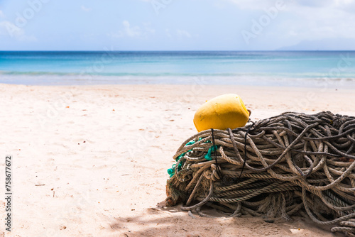 Old fishing nets with yellow float lay on white sand of Beau Vallon Beach