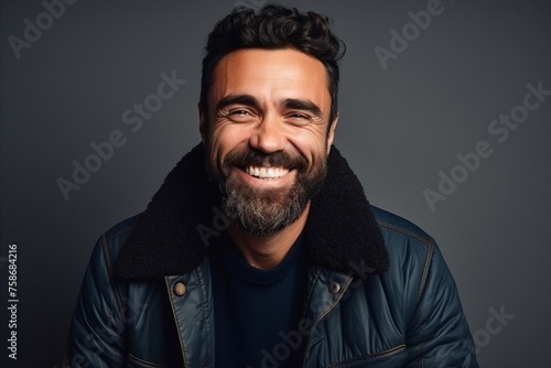 Portrait of a smiling bearded man in a leather jacket over grey background. © Igor