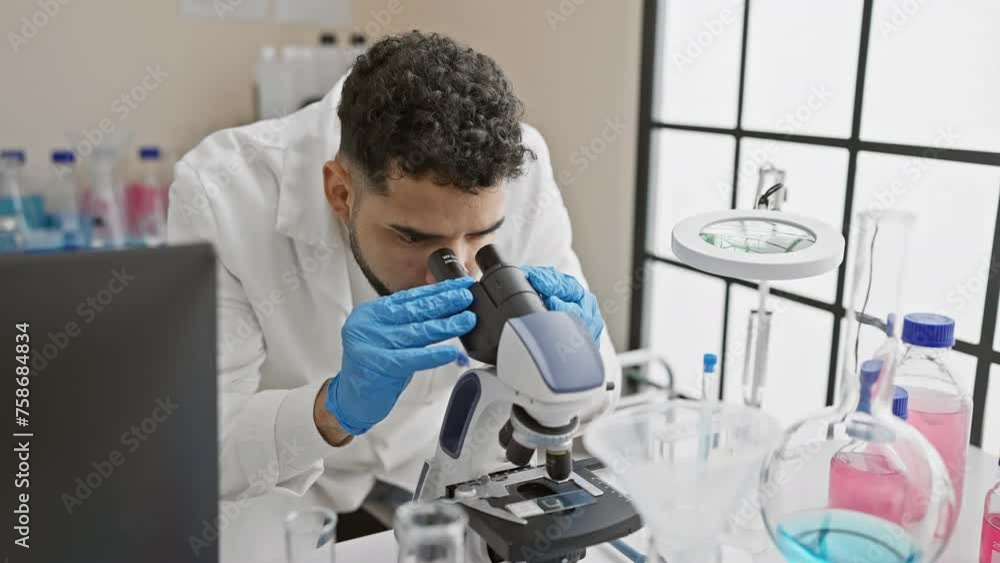 A young hispanic man with a beard works in a laboratory, using a microscope, portraying a professional healthcare setting. A young hispanic man with a beard works in a laboratory, using a microscope, portraying a professional healthcare setting.