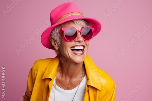Portrait of happy senior woman in sunglasses and hat over pink background