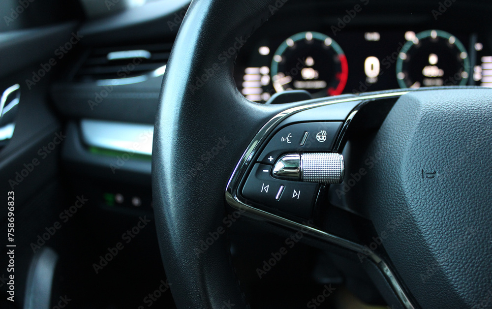 Defocused backlight of LED dashboard behind car steering wheel with heating and voice control buttons on it
