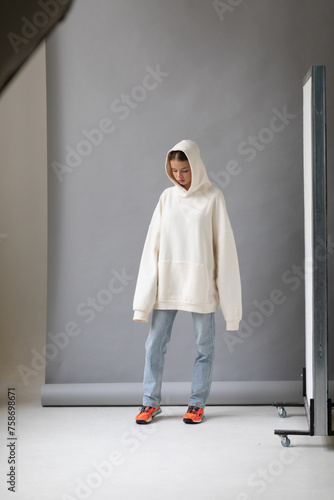 Beautiful blonde woman in a white hoodie and blue jeans posing on a gray background