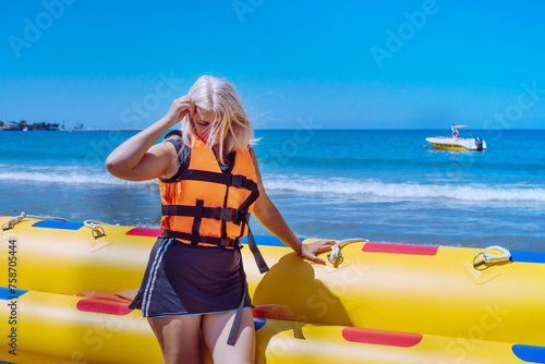 Blonde woman in a life jacket on the beach near the sea. Summer vacation concept