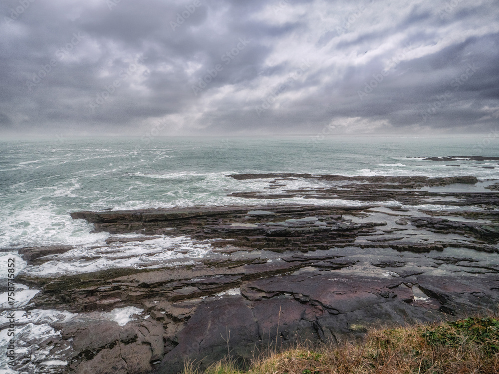 Obraz premium Rough stone coastline and powerful waves of the ocean. Mullaghmore, county Sligo, Ireland. Popular tourist area with stunning nature scenery. Dramatic low cloudy sky. Irish landscape landmark