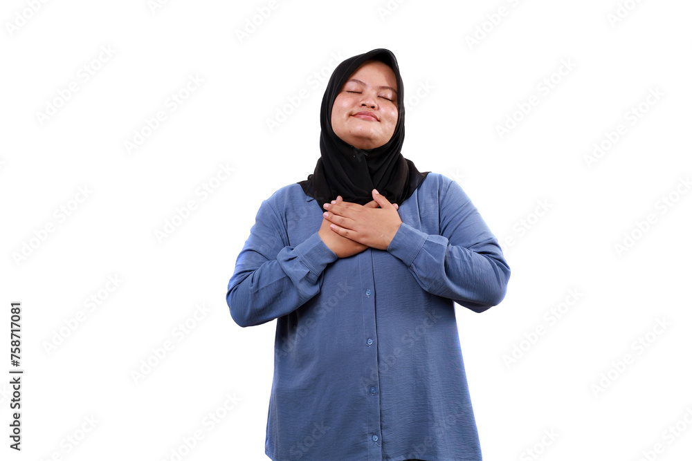 Relieved asian muslim woman standing touching her chest while closing her eyes Relieved asian muslim woman standing touching her chest while closing her eyes