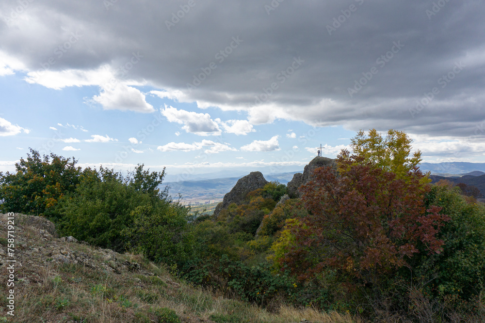 Landscape view from the ruins of Kojori fortress. Bright blue sky and clouds. Mountains, rocks, villages in the valley and a line of clouds on the horizon. Colored bushes and green grass.