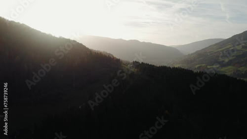 Drone circling around an autumn colored forest in the mountains, with the sun slowly piercing through the mist in the background photo