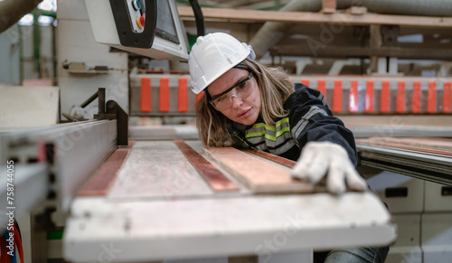 Confident female engineer working in lumber warehouse of hardwood furniture factory inspecting production machine. Serious female technician, carpenter busy working with tool in woodwork manufacturing