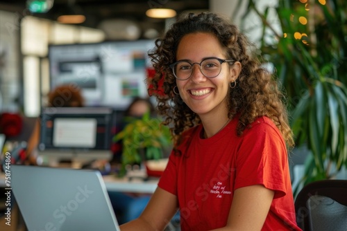 Portrait of successful businesswoman at workplace inside office, woman smiles and looks at camera, uses laptop at work, female programmer in red shirt with curly hair, codes new software,Generative AI photo