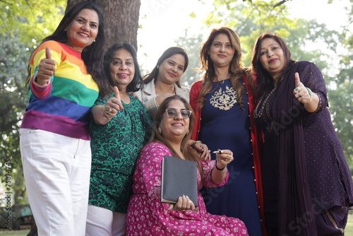 Portrait of mid aged women holding a black color almanac in hand, sunlight, green park serene environment. woman leaning against tree. ladies promoting a book. blank book cover.