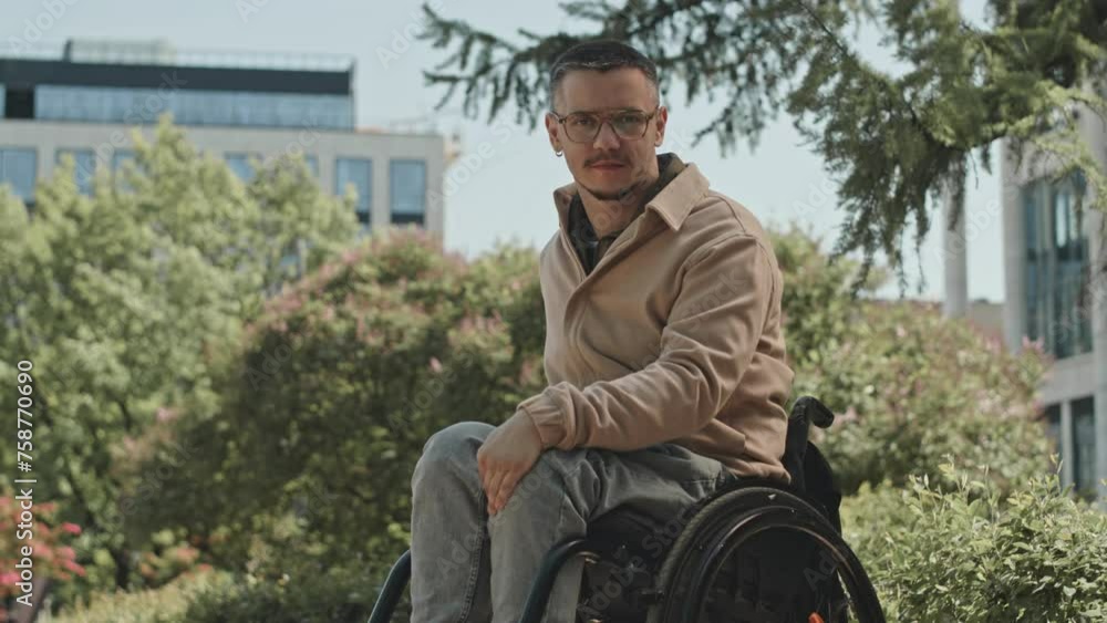 Young man in wheelchair posing for camera outdoors during sunny day in park Young man in wheelchair posing for camera outdoors during sunny day in park
