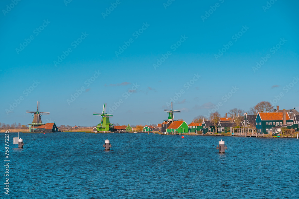 Beautiful Dutch scenery panorama of Zaanse Schans village in Netherlands in spring time. Ancient windmills at the water's edge in the background with the blue sky in sunny weather