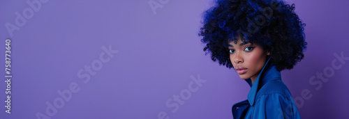A woman with blue hair and a blue shirt is standing in a field of purple flowers. model with blue afro hair wearing a blue trench in a full body photoshoot like wild flower composition blue and purple