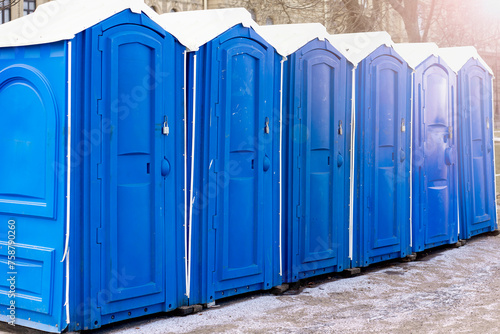 Row of blue clean outdoor portable toilets in winter with bright blue doors and white roof at urban street photo