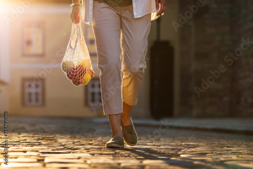 Woman walks on street and carrying reusable mesh bag with apple fruits. Plastic free and zero waste sustainable shopping lifestyle