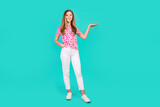 Full body photo of pretty teenager girl palm hold empty space dressed stylish pink print clothes isolated on aquamarine color background