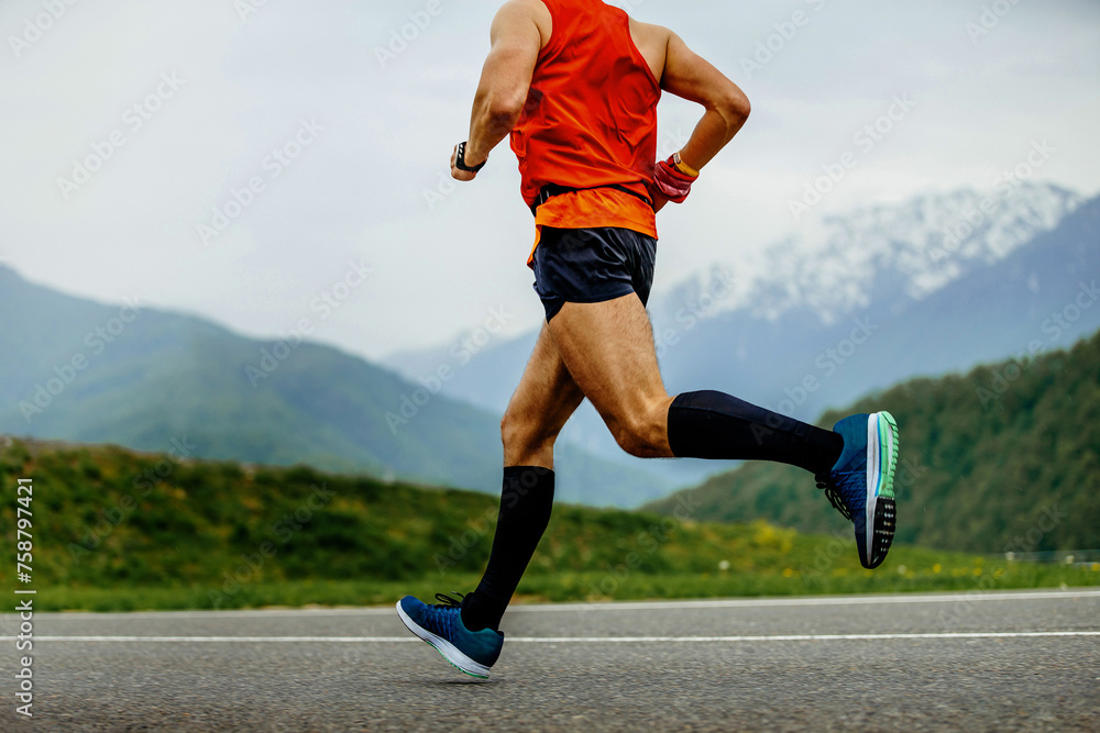 male athlete running mountain marathon on asphalt in black compression socks male athlete running mountain marathon on asphalt in black compression socks