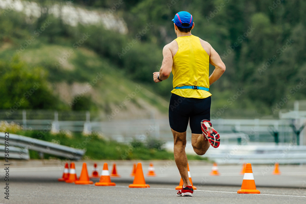Fototapeta premium rear view athlete running on asphalt with orange safety cones, mountain marathon race