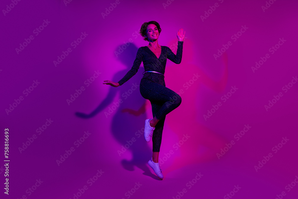 Full length photo of lovely young lady wave hand jumping wear trendy overall garment isolated on neon light pink color background