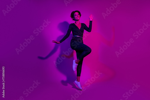 Full length photo of lovely young lady wave hand jumping wear trendy overall garment isolated on neon light pink color background © deagreez