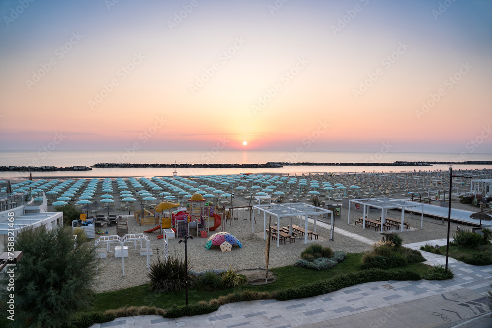 Beautiful sunrise on Rimini beach with umbrellas
