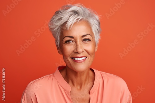 Portrait of smiling senior woman with grey hair on orange background.