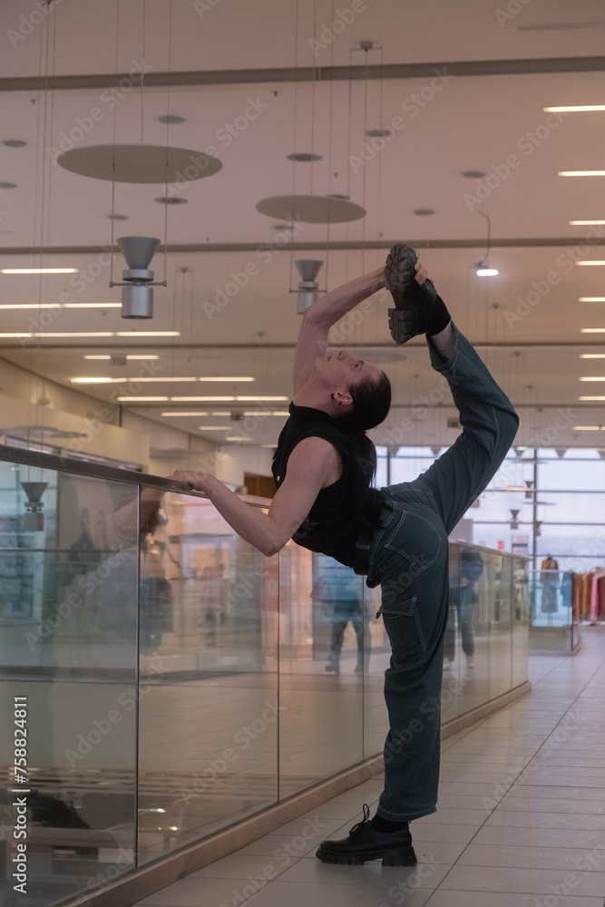 Fototapeta premium A young androgynous teenage male dancer doing acrobatic dancing poses indoors in a shopping center