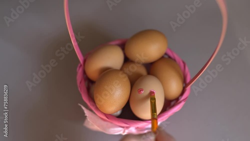 Close-up of a hand painting a smiley face with a brush on an egg. Easter tradition of painting eggs. Eggs in a basket are a symbol of Easter.