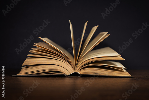 Open old book lying on a wooden table. Dark background