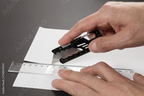 Man cuts paper with a stationery knife and ruler close up