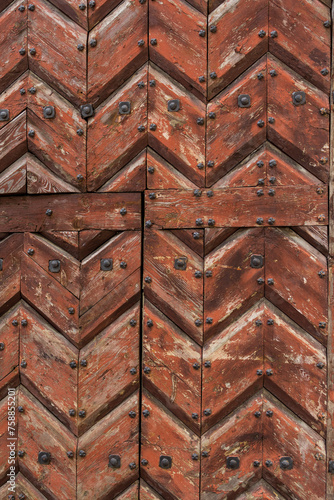 wooden brown painted door composed of zigzag planks placed. it is a lining that is nailed with metal rivets or nails © elenarostunova