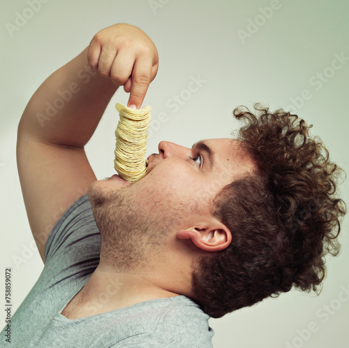 Overweight, eating and man with chips in studio for unhealthy, potato and salty snack. Plus size, food and profile of male person enjoying stack of crisps in mouth isolated by gray background. photo