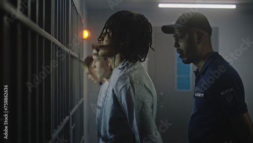 Fotografie Group of teen prisoners stand in front of jail cells, warden talks with them
