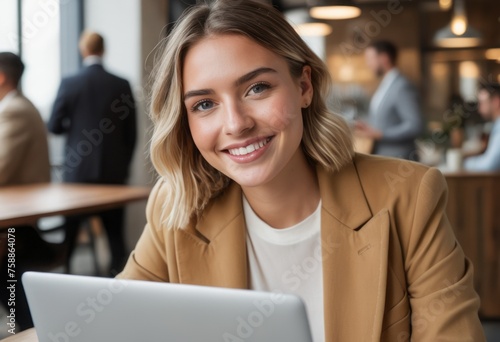 A smiling woman working on her laptop in a bustling office environment. She looks professional and pleased with her work. © natakot