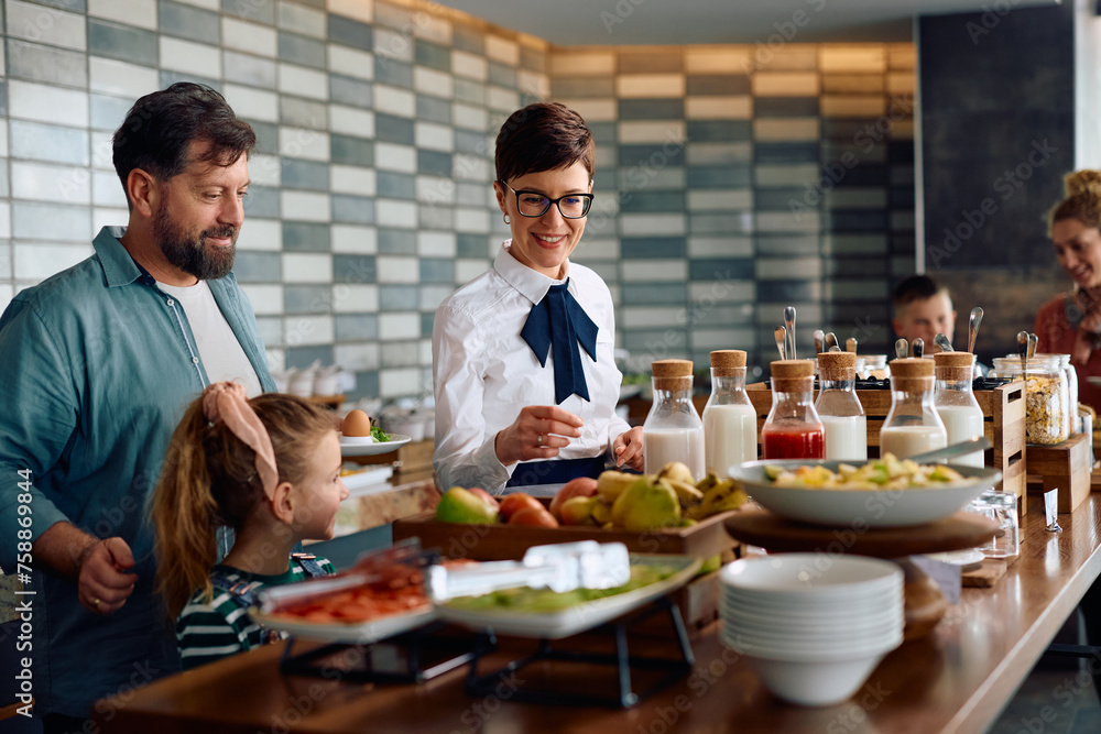 Happy waitress serving breakfast to family at buffet table in hotel. Happy waitress serving breakfast to family at buffet table in hotel.