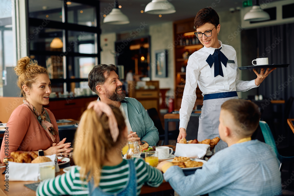Happy waitress talking to family while serving them during breakfast at hotel restaurant. Happy waitress talking to family while serving them during breakfast at hotel restaurant.