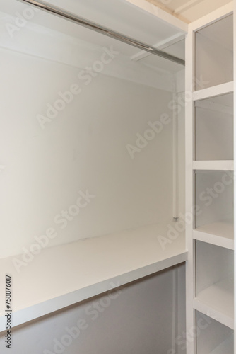 Interior white solid wood closet with wood shelves and a clothing bar