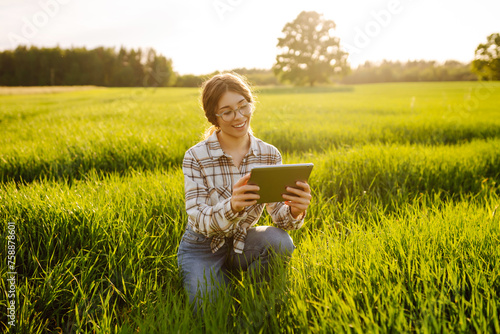 Woman Farmer on a green wheat field with a tablet in his hands. Smart farm. The concept of the agricultural business.