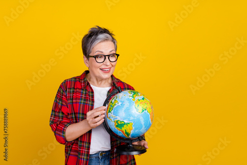 Portrait of cheerful aged lady look arms hold planet earth globe empty space isolated on yellow color background