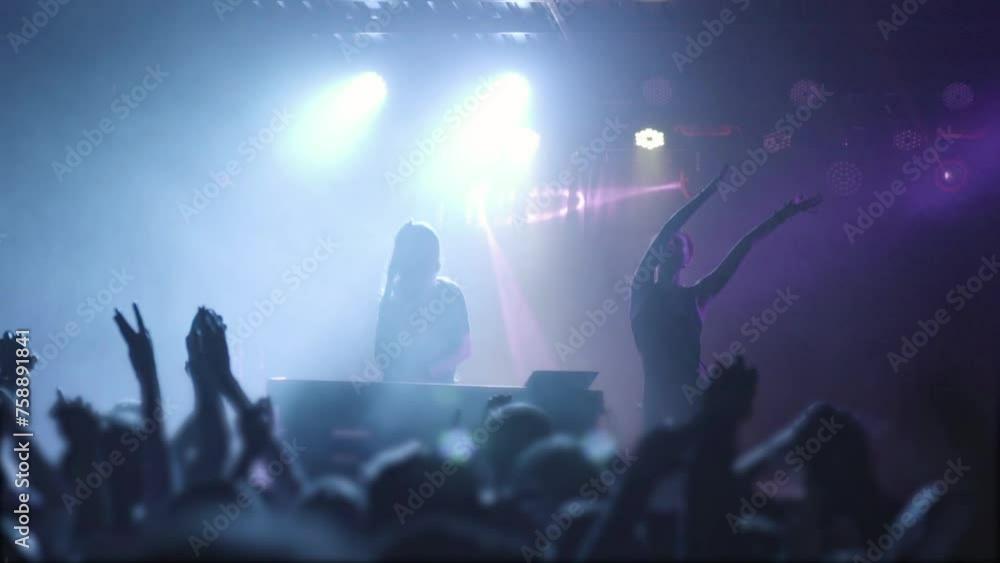 Two beautiful young women DJ play the music on the mixing console in the nightclub. Against the background of unrecognizable people. Slow motion Two beautiful young women DJ play the music on the mixing console in the nightclub. Against the background of unrecognizable people. Slow motion