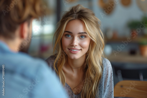 A young woman with blond hair communicates affably with a smile on a date with a young man out of focus. Dialogue and relationship concept