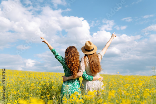 Two young women in a beautiful field with yellow flowers. They jump and have fun. Friendship Day