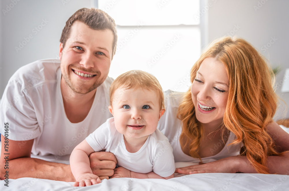 Mother father and baby boy on bed, having great moment together on white bedroom Mother father and baby boy on bed, having great moment together on white bedroom