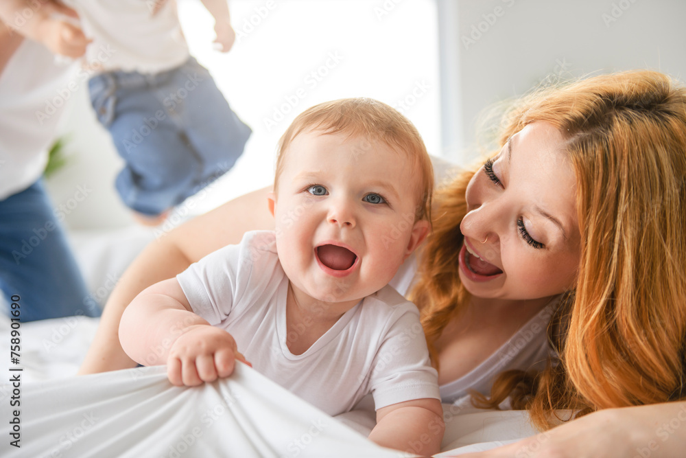 Mother and baby boy on bed, having great moment together on white bedroom Mother and baby boy on bed, having great moment together on white bedroom